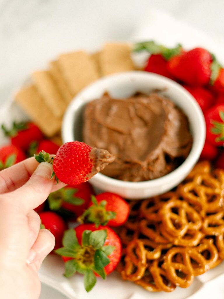 A hand holding a fresh strawberry that has been dipped into the finished Nutella Fruit Dip.