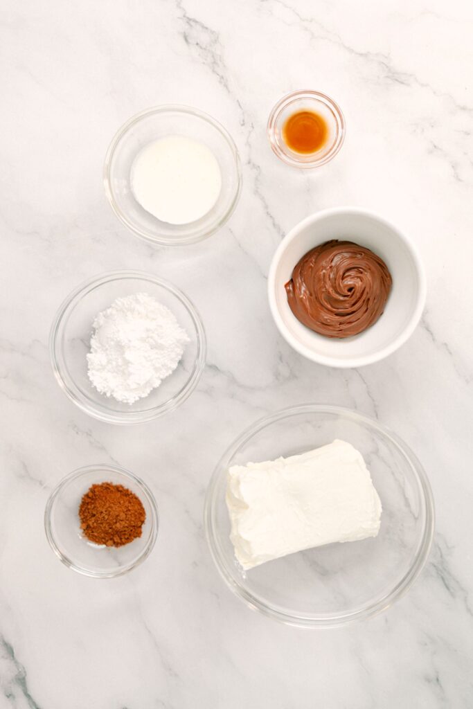 Flat lay shot of the ingredients for the Nutella Fruit Dip such as a block of cream cheese, whipping cream, powdered sugar, cocoa powder, vanilla extract and Nutella.