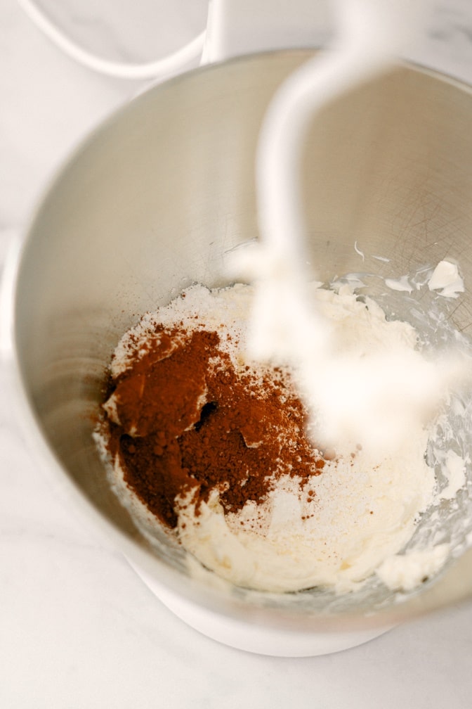 High angle shot of a mixing bowl with whipped cream cheese, with powdered sugar and cocoa powder added to it.