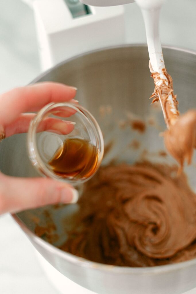 A hand about to pour vanilla from a small glass bowl and into the Nutella Fruit Dip.