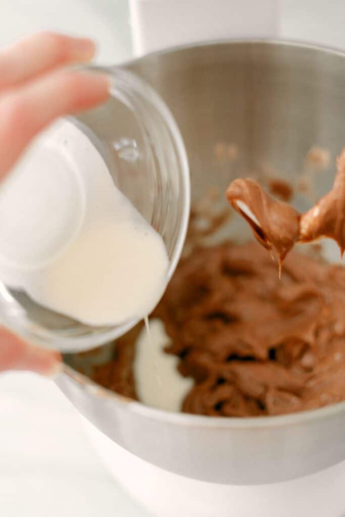A hand pouring whipped cream from a glass bowl and into the Nutella Fruit Dip mixture.