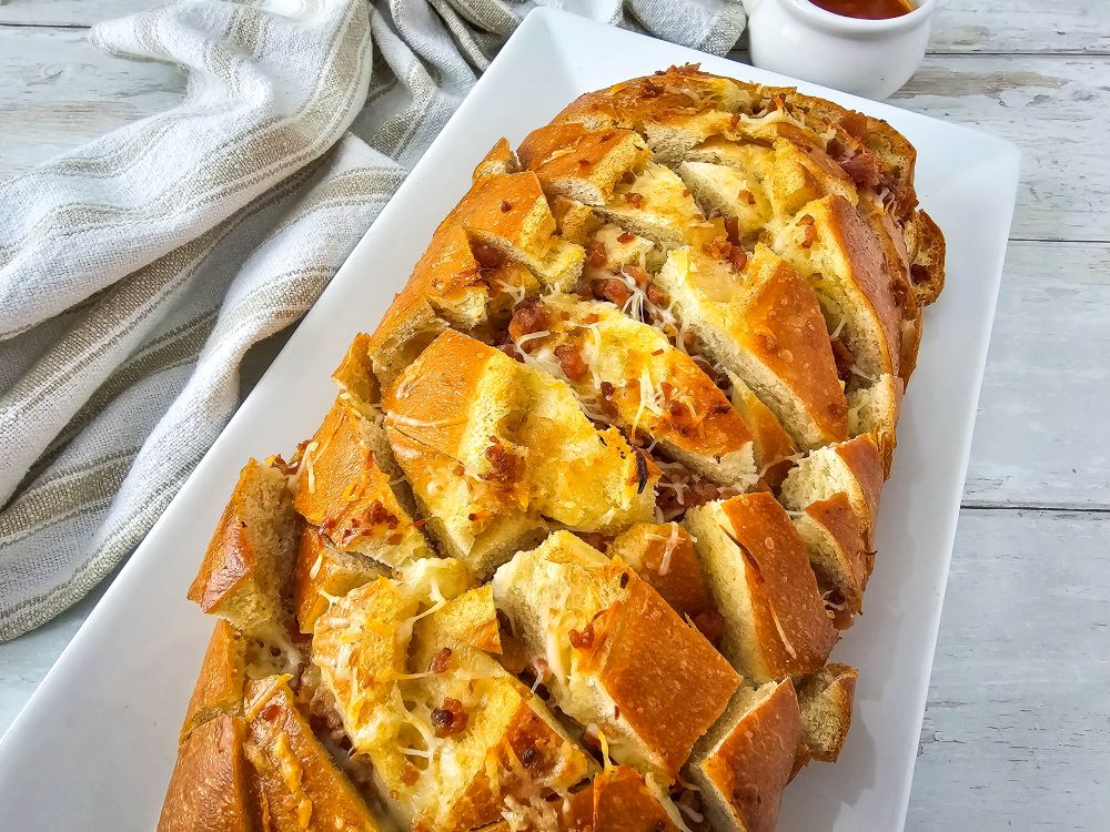 Overhead shot of the finished Cheesy Bacon Pull Apart bread on a white rectangular platter.