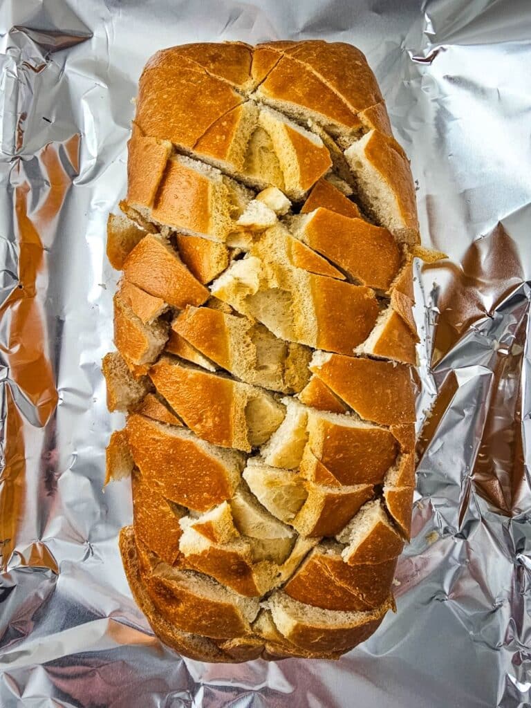 Flat lay shot of a loaf of bread with criss-cross slices across its surface. The loaf is then placed on a tray lined with aluminum foil.