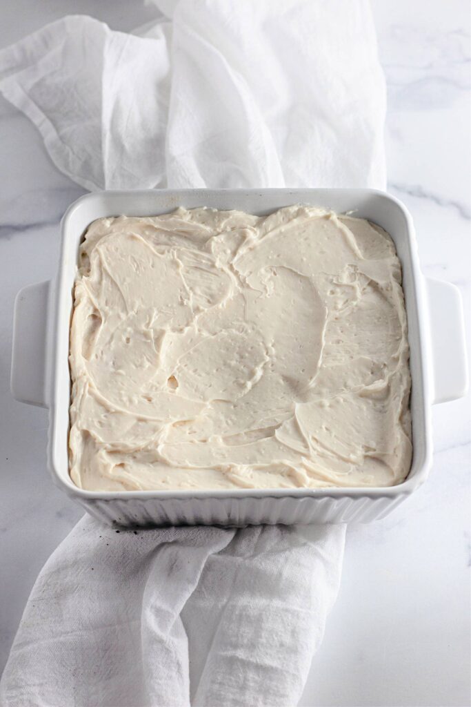 Strawberry Shortcake Crunch Bars with Box Cake Mix 13 A square baking dish with white cream cheese frosting in it.
