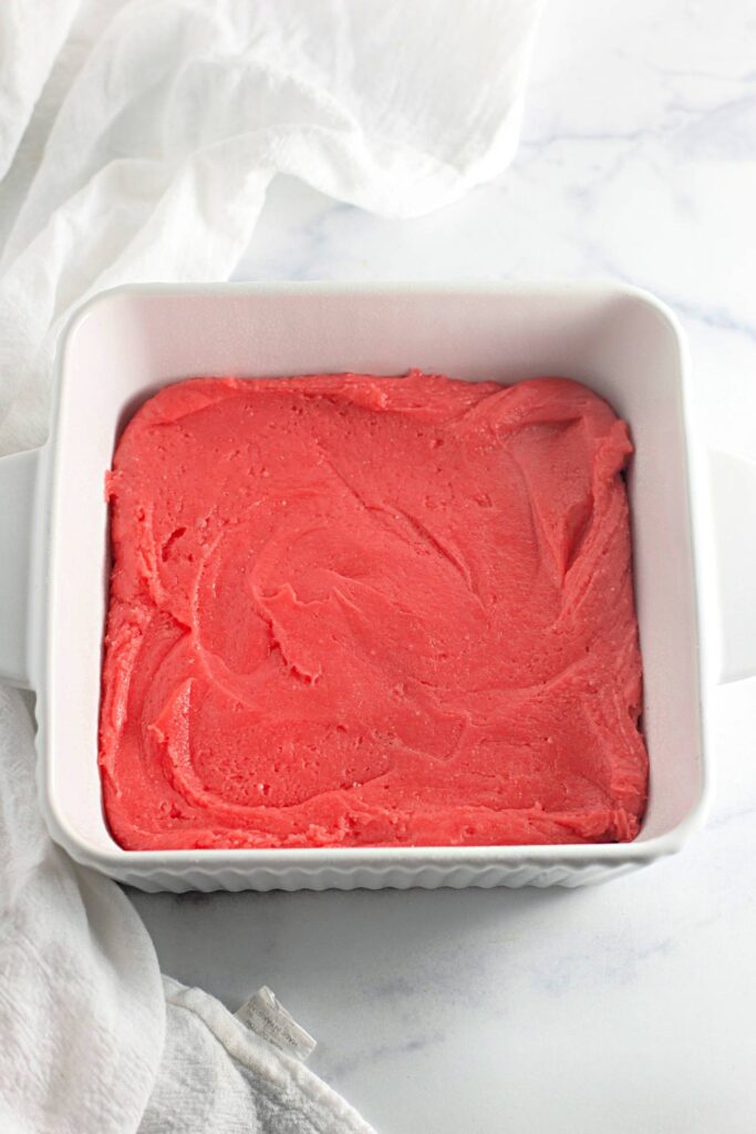 Strawberry Shortcake Crunch Bars with Box Cake Mix 9 A pink cake batter spread evenly on a square white baking dish.