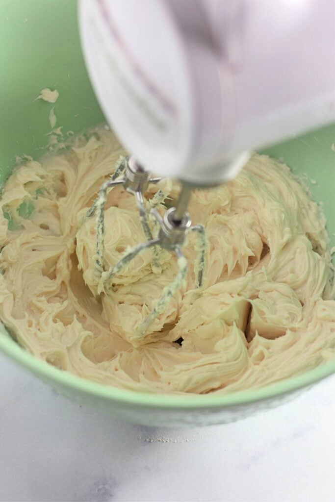 Strawberry Shortcake Crunch Bars with Box Cake Mix 11 Hi angle shot of a green mixing bowl with cream cheese frosting being whipped with a handheld mixing.