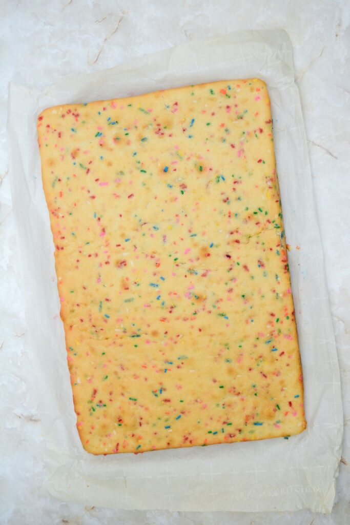 A colorful baked sheet cake on a sheet of parchment paper.