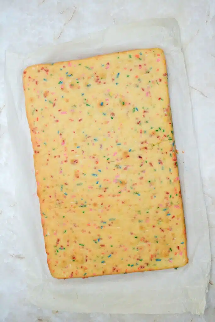 Easy From Scratch Confetti Birthday Cake Roll Recipe with Cream Cheese Frosting 19 A colorful baked sheet cake on a sheet of parchment paper.