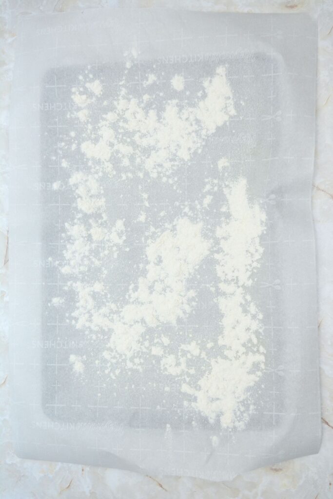 Flat lay shot of a parchment paper on a sheet tray, with flour sprinkled deliberately on it.