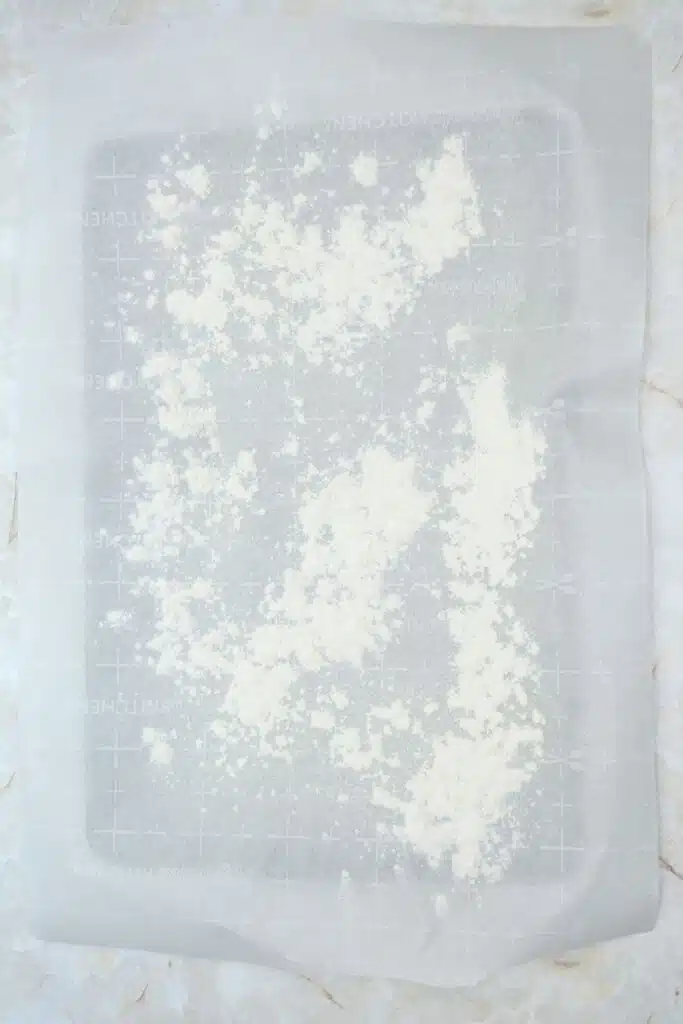 Easy From Scratch Confetti Birthday Cake Roll Recipe with Cream Cheese Frosting 18 Flat lay shot of a parchment paper on a sheet tray, with flour sprinkled deliberately on it.
