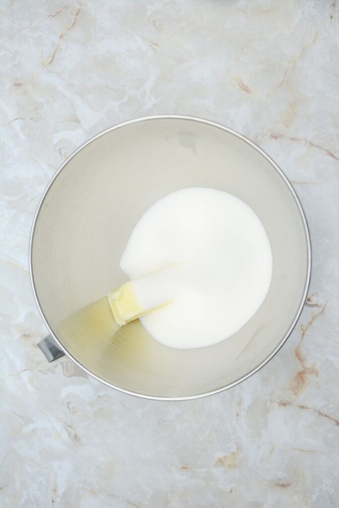 Flat lay shot of a mixing bowl with white granulated sugar and a stick of butter in it.