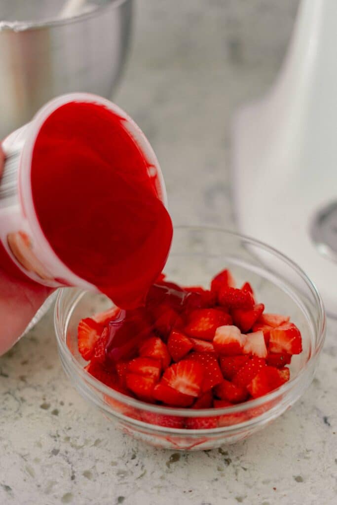 Best No-Bake Strawberry Cream Cheese Pie 11 A hand pouring strawberry glaze into a bowl of chopped strawberries.