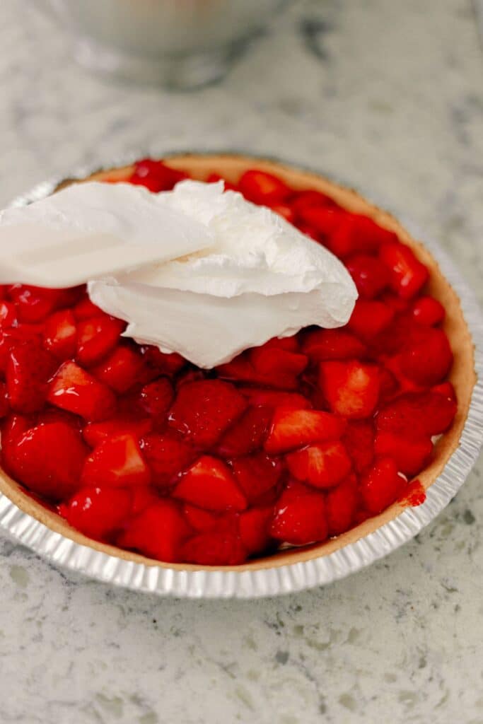 Best No-Bake Strawberry Cream Cheese Pie 14 Dollops of cream cheese frosting on top of a layer of chopped strawberries in a pie dish.