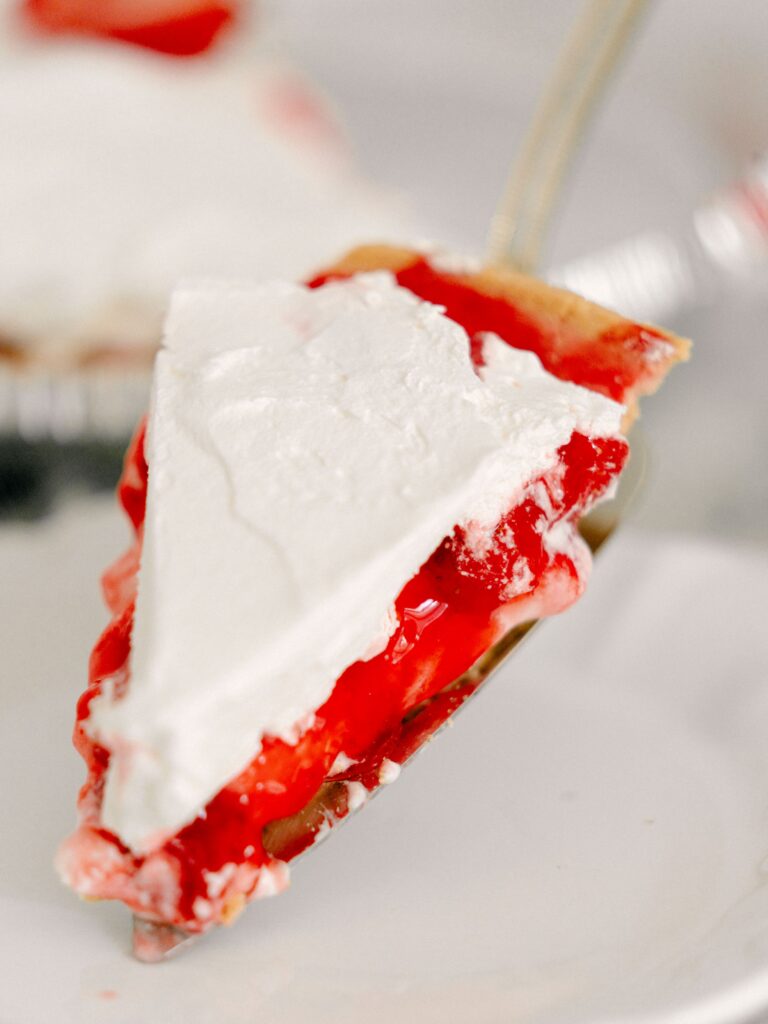 Best No-Bake Strawberry Cream Cheese Pie 6 A slice of The No-Bake Strawberry Cream Cheese Pie on a cake server, about to be placed on a white dessert plate.