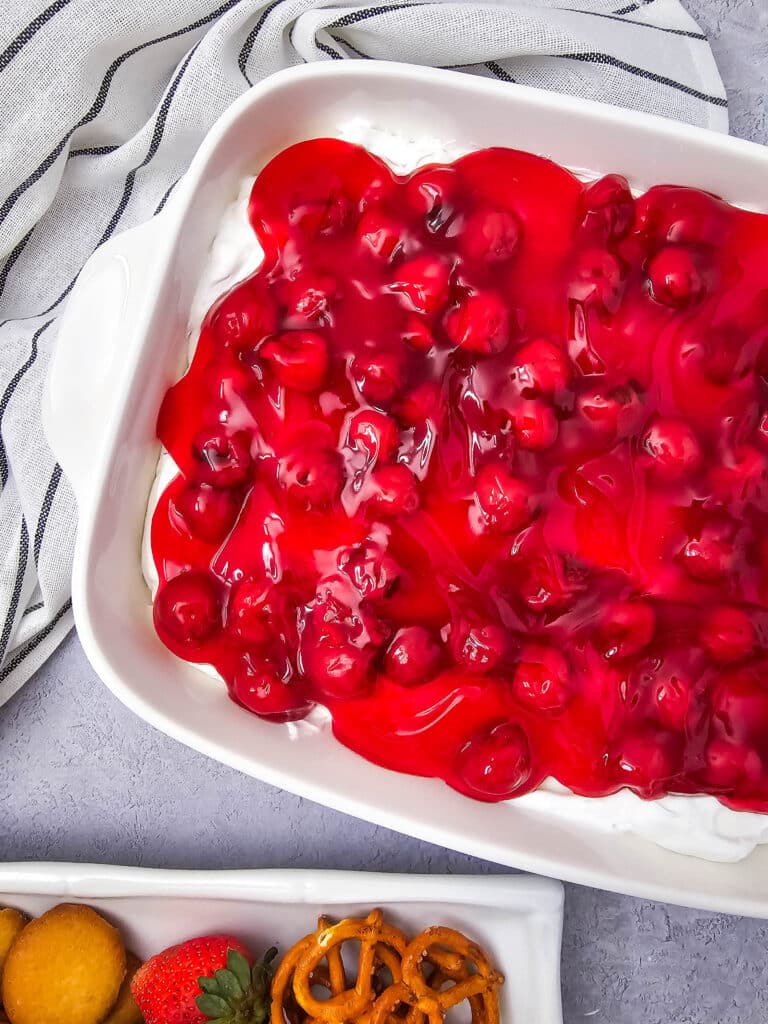 Easy 4-Ingredient Cherry Cheesecake Dip 4 Flat lay shot of the Easy 4-Ingredient Cherry Cheesecake Dip in a white serving dish. Next to it is a platter with assorted dippers such as mini pretzels, vanilla wafers and fresh strawberries.