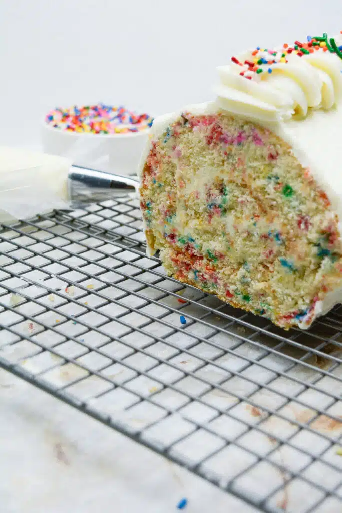 Easy From Scratch Confetti Birthday Cake Roll Recipe with Cream Cheese Frosting 33 A Confetti Cake Roll on a wire rack with its end sliced to reveal its colorful interior.