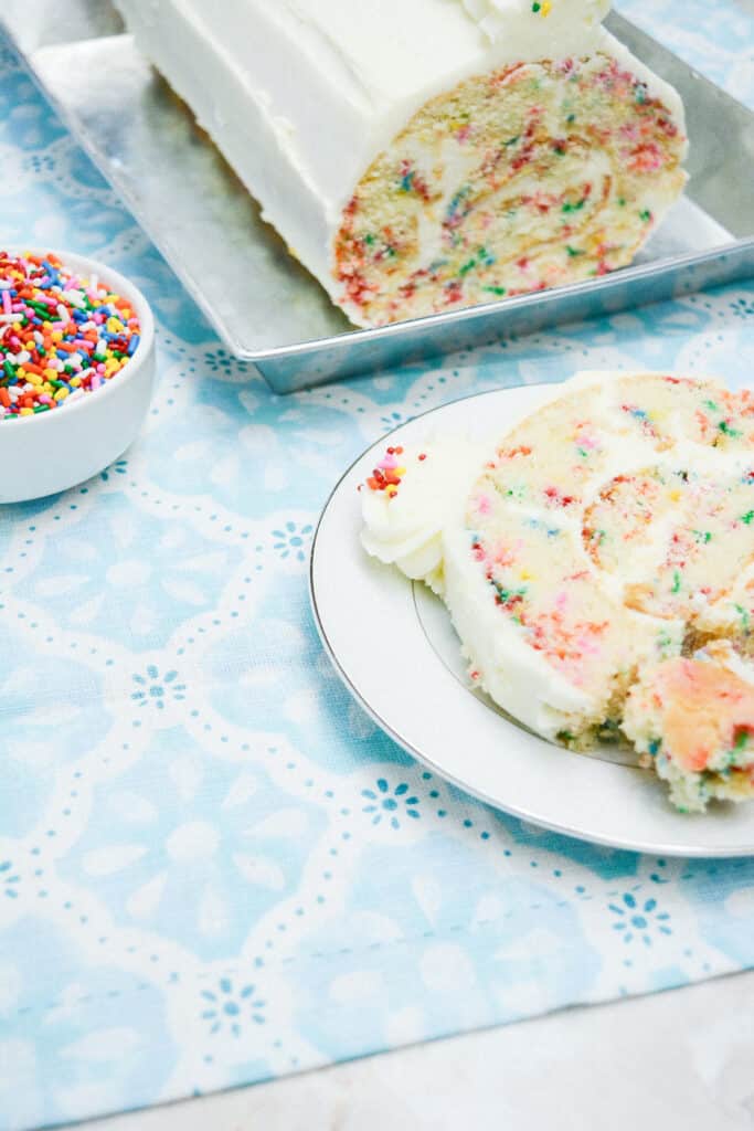 A partial shot of the Delightful Funfetti Birthday Cake Roll slice on a white dessert plate.