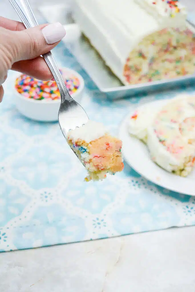 Easy From Scratch Confetti Birthday Cake Roll Recipe with Cream Cheese Frosting 6 A hand holding a fork with a piece of the Delightful Funfetti Birthday Cake Roll in it.