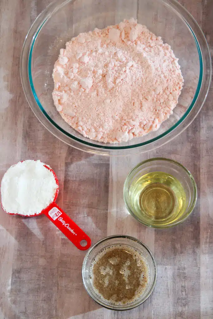 The Easiest Strawberry Cake Mix Crinkle Cookies (4 Ingredients + Vegan!) 5 Flat lay shot of the ingredients for the cookies such as a bowl of pink cake mix, a cup of powdered sugar, a small bowl with vegetable oil, and another bowl with flax eggs.