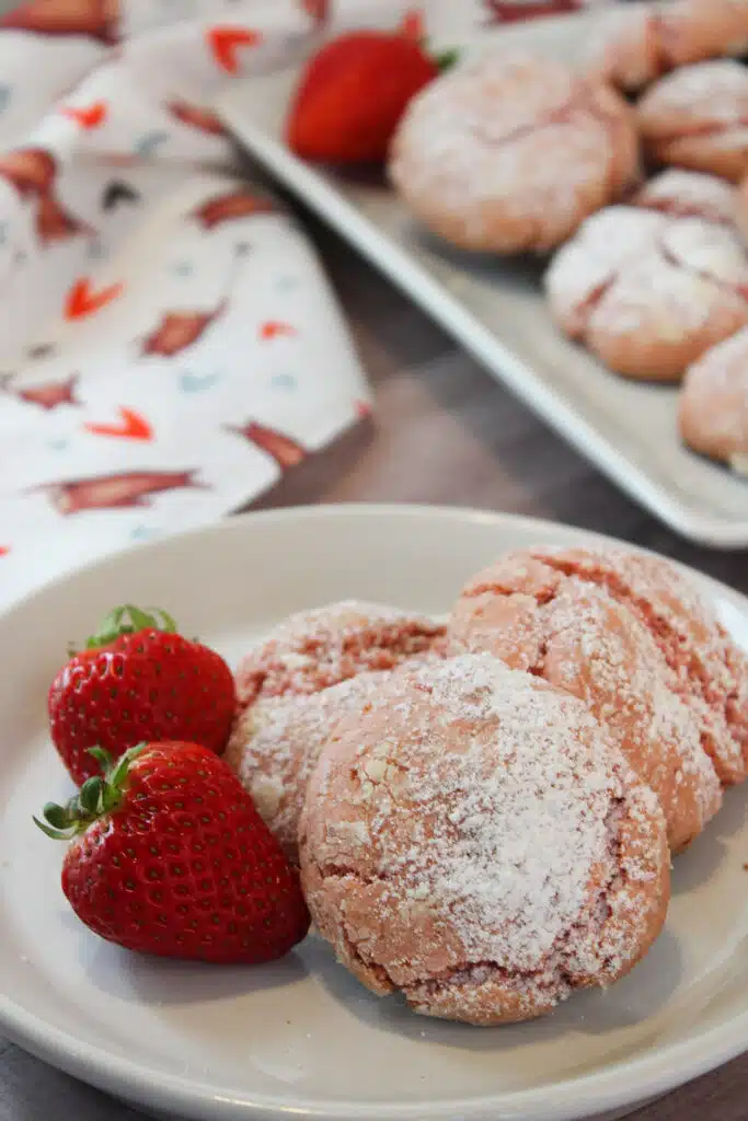 The Easiest Strawberry Cake Mix Crinkle Cookies (4 Ingredients + Vegan!) 3 Three 4-Ingredient Vegan Strawberry Cake Mix Crinkle Cookies with 2 fresh strawberries beside them.