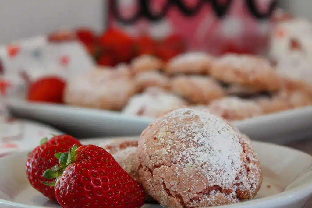 The Easiest Strawberry Cake Mix Crinkle Cookies (4 Ingredients + Vegan!) 14 Strawberry Crinkle Cookies on white plate next to fresh strawberries.