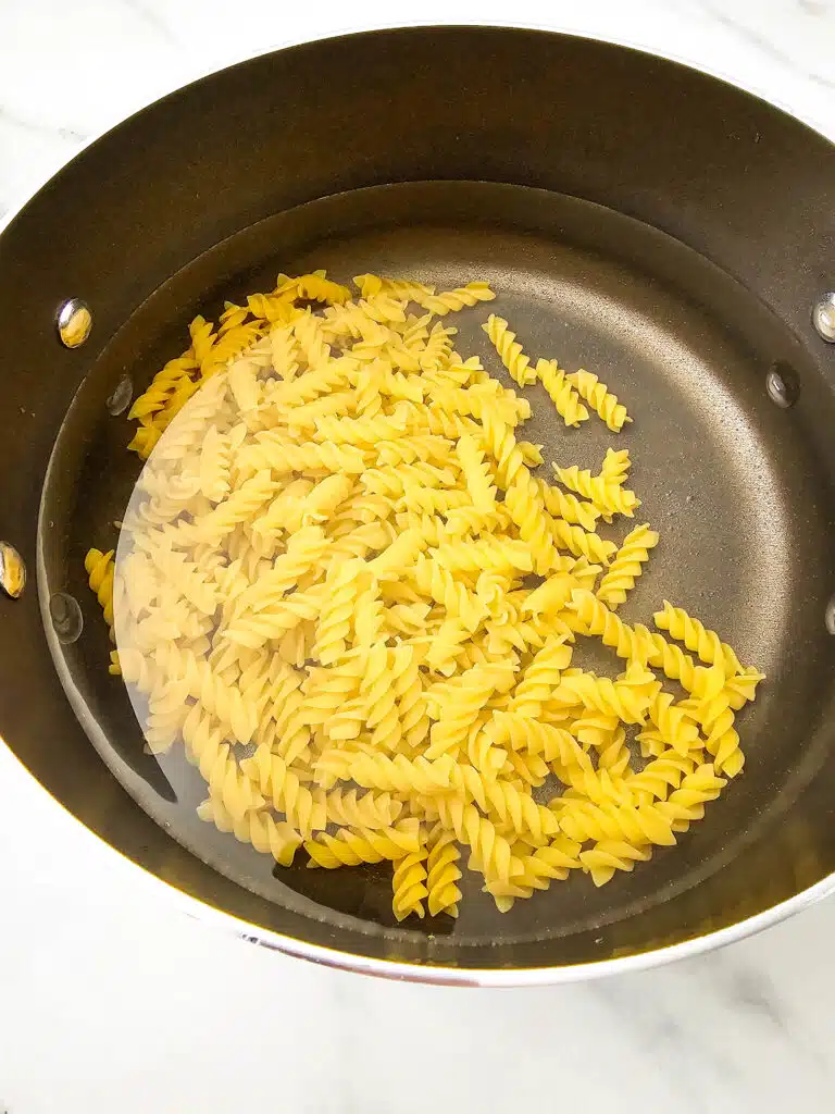 A pot with water and rotini pasta in it.