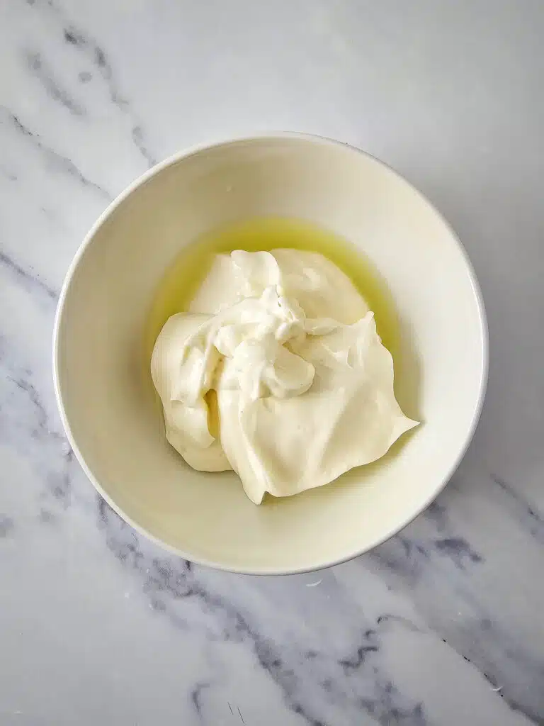 A white bowl with lime juice topped with mayonnaise.