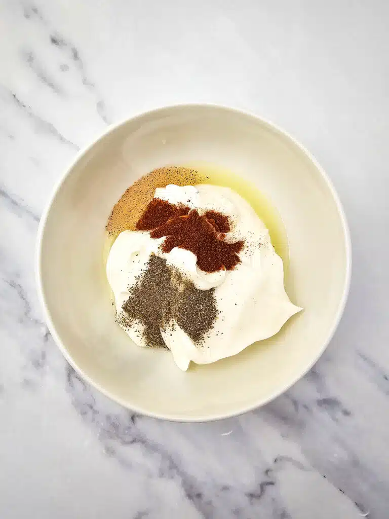Flat lay shot of a white bowl with lime juice, mayonnaise, black pepper, salt and chili powder.