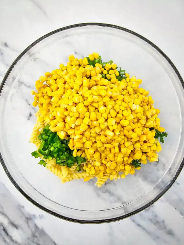 Sweet corn added into the rotini and vegetable mixture in the glass bowl.
