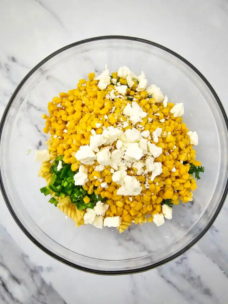 Crumbled Cotija cheese added into the salad mixture in the glass bowl.
