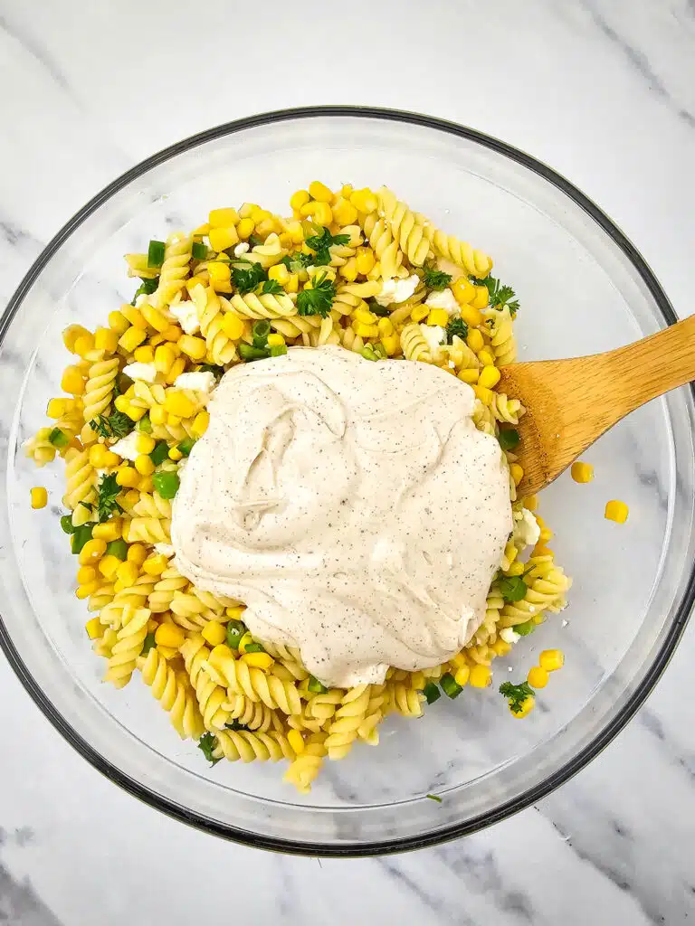 A glass bowl with the Mexican Street Corn Pasta Salad topped with the dressing.