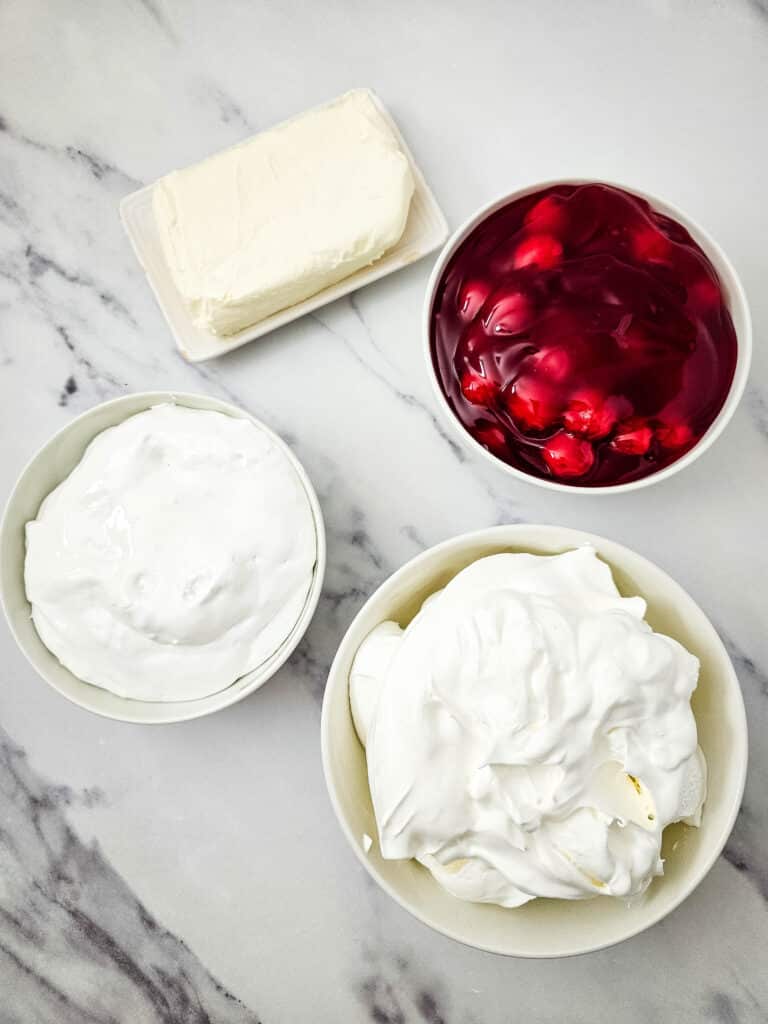 Easy 4-Ingredient Cherry Cheesecake Dip 5 Flat lay shot of the ingredients for the Cherry Cheesecake Dip such as cherry pie filling, cool whip, cream cheese and marshmallow fluff. Each ingredient are on separate bowls in a marble surface.