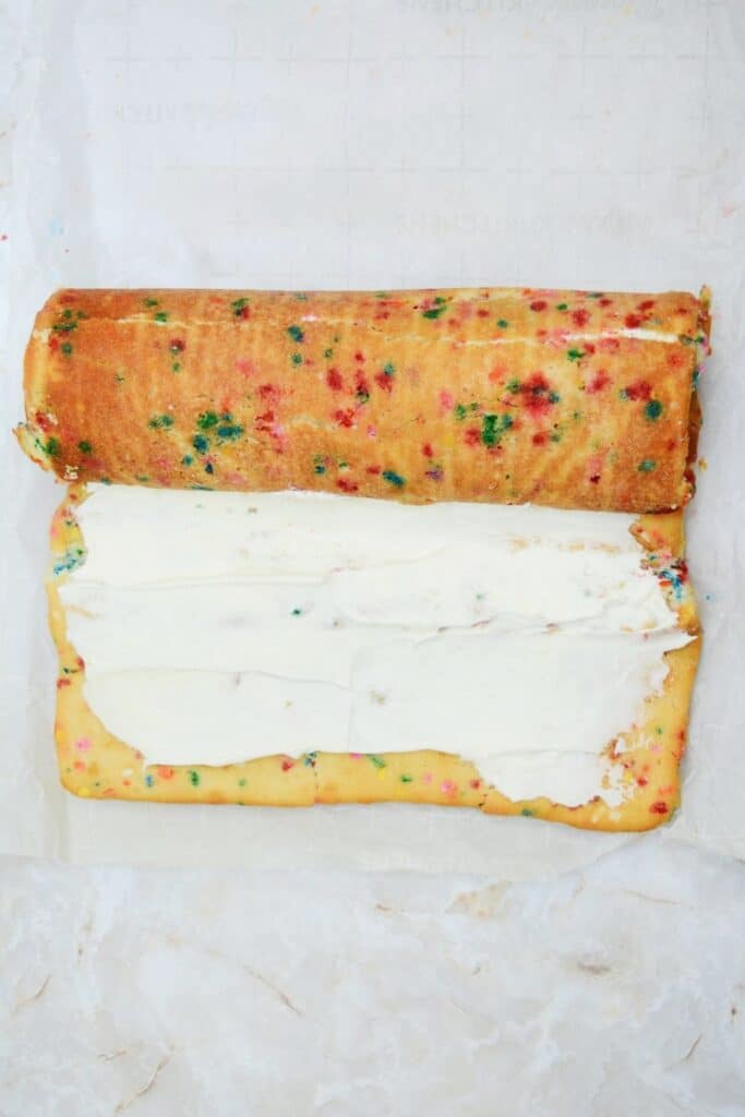 The frosted sheet cake rolled halfway through on a marble surface.