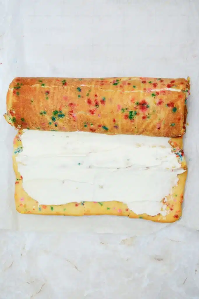 Easy From Scratch Confetti Birthday Cake Roll Recipe with Cream Cheese Frosting 26 The frosted sheet cake rolled halfway through on a marble surface.