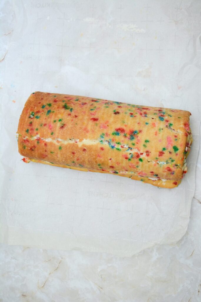 A rolled Funfetti cake with a sheet of parchment paper underneath it.
