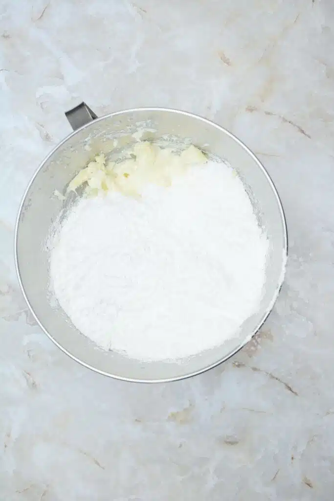 Easy From Scratch Confetti Birthday Cake Roll Recipe with Cream Cheese Frosting 23 Flat lay shot of a mixing bowl with whipped cream and powdered sugar in it.