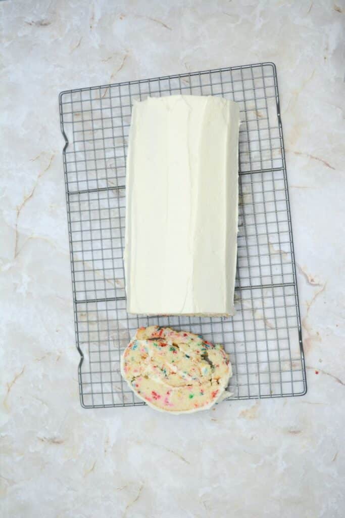 A slice of the Delightful Funfetti Birthday Cake Roll beside the rest of the roll cake on a wire rack.