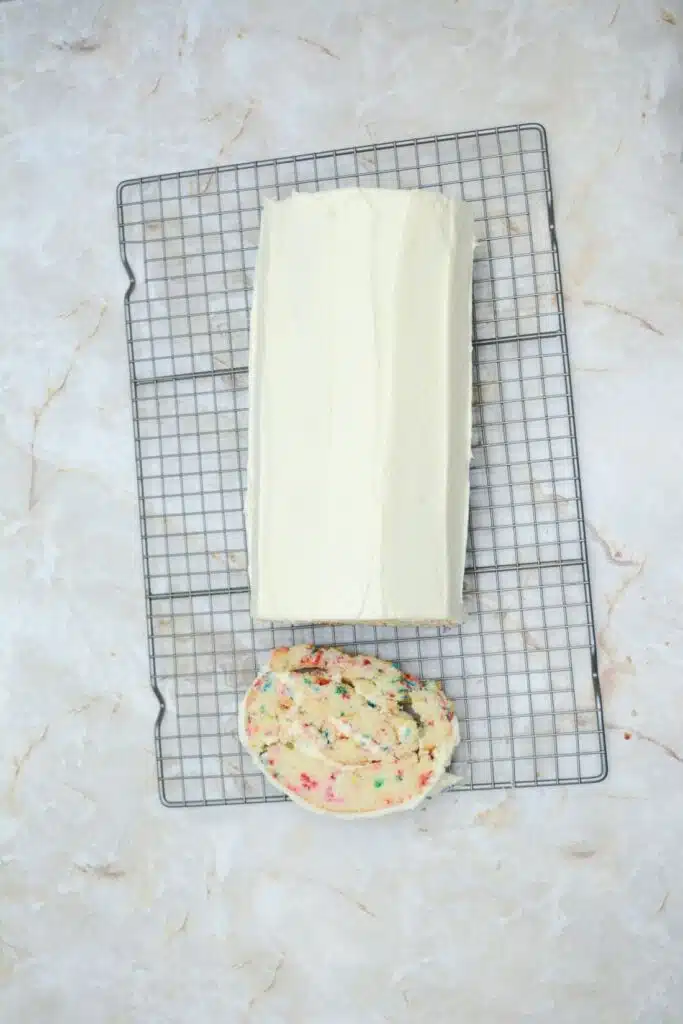 Easy From Scratch Confetti Birthday Cake Roll Recipe with Cream Cheese Frosting 29 A slice of the Delightful Funfetti Birthday Cake Roll beside the rest of the roll cake on a wire rack.
