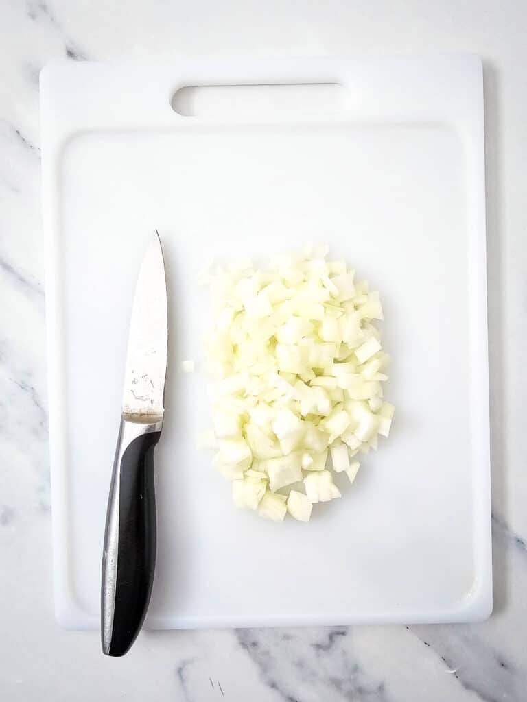 Diced yellow onion on a white chopping board, with a small knife beside it.