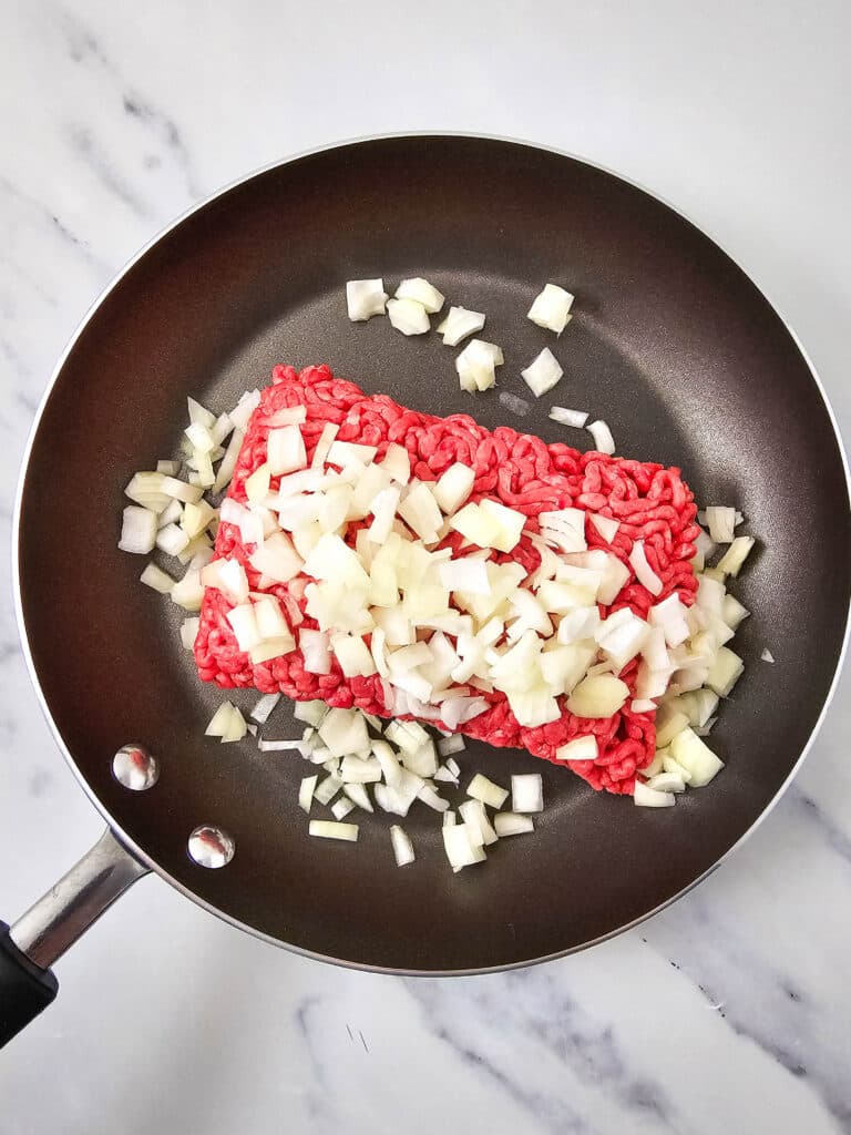 A skillet with raw ground venison and diced onions in it.