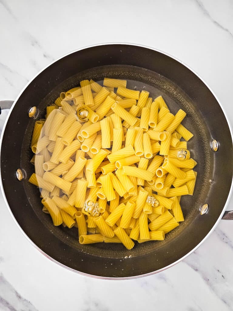 A pot with water and rigatoni pasta in it.
