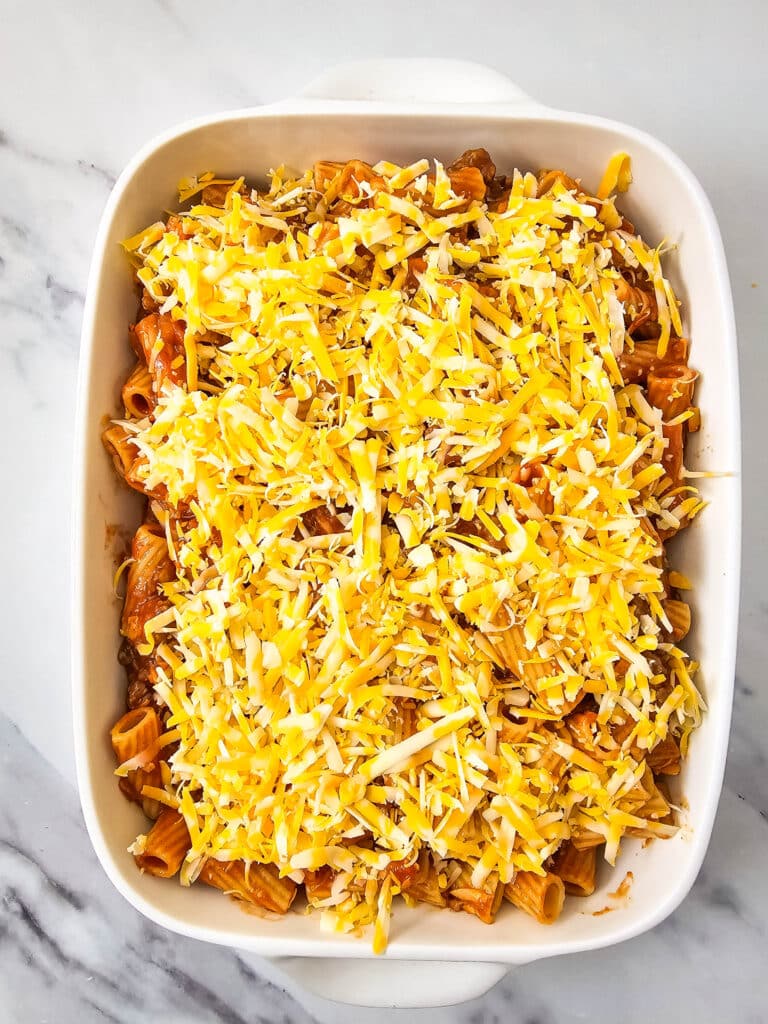 Flat lay of a white baking dish with the pasta dish in it. It's then topped with shredded yellow cheese.