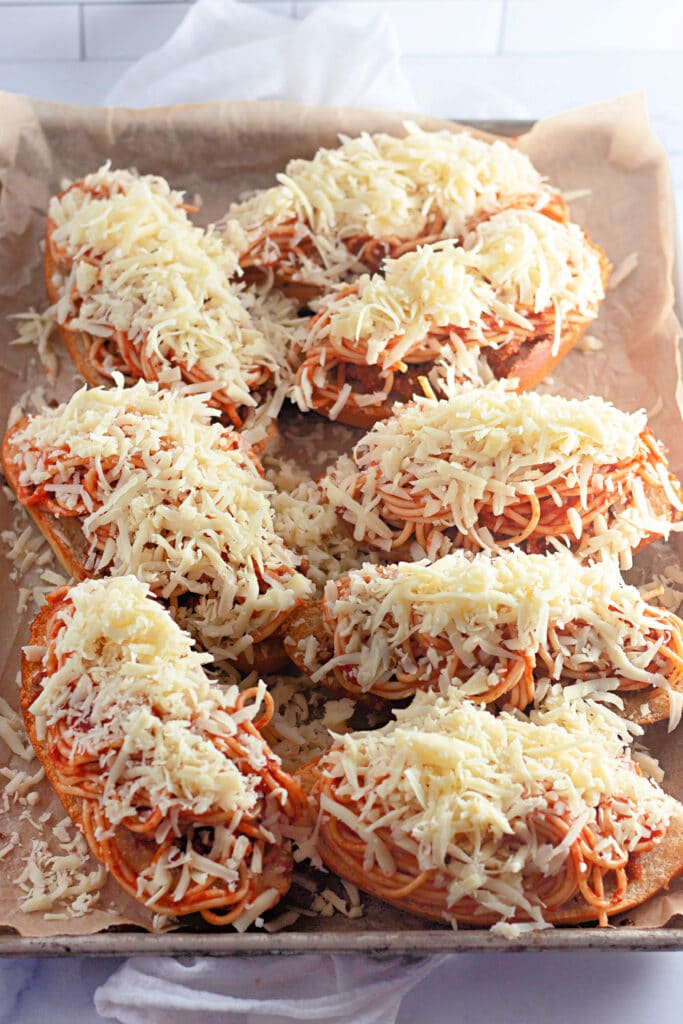 Venison Spaghetti Bread (A Family Favorite!) 16 Eight Venison Spaghetti Breads topped with generous amounts of shredded cheese, on a sheet tray.