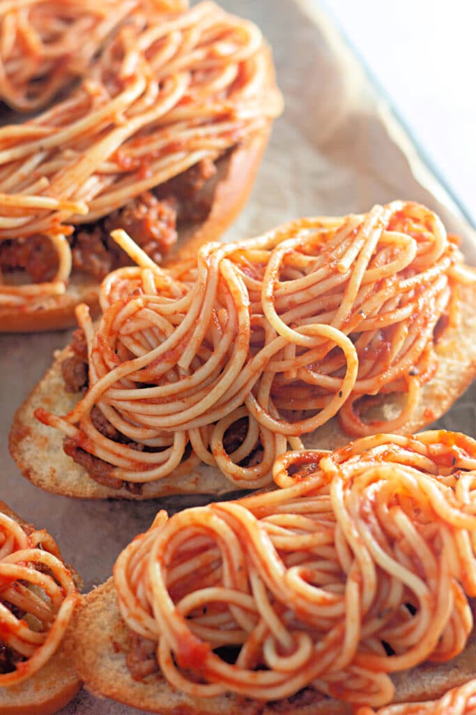Venison Spaghetti Bread (A Family Favorite!) 15 Closeup shot of a sheet tray with halved Hoagie rolls topped with meat sauce and spaghetti.
