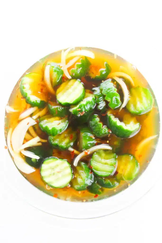 Flat lay shot of a glass bowl with the Easy Refrigerator Bread and Butter Pickles.