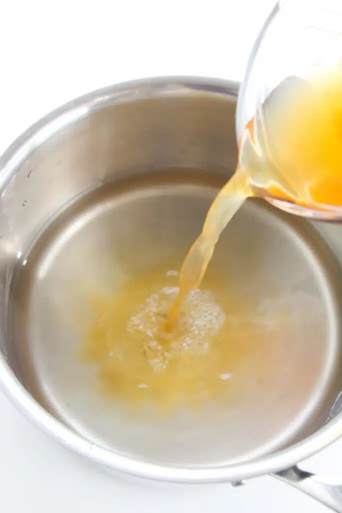 Apple cider vinegar being poured into a small saucepan with distilled vinegar in it.