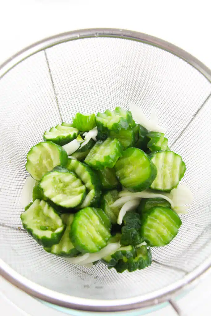 Salted cucumbers and onions rinsed in a strainer.