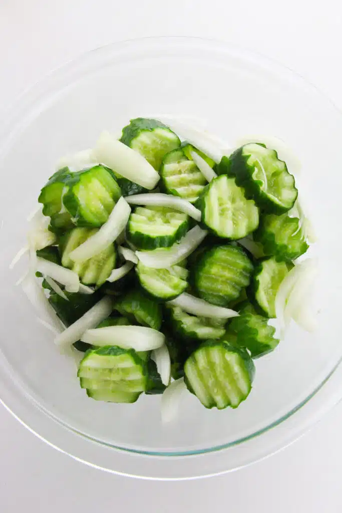 A glass bowl with cucumbers and sliced onions.