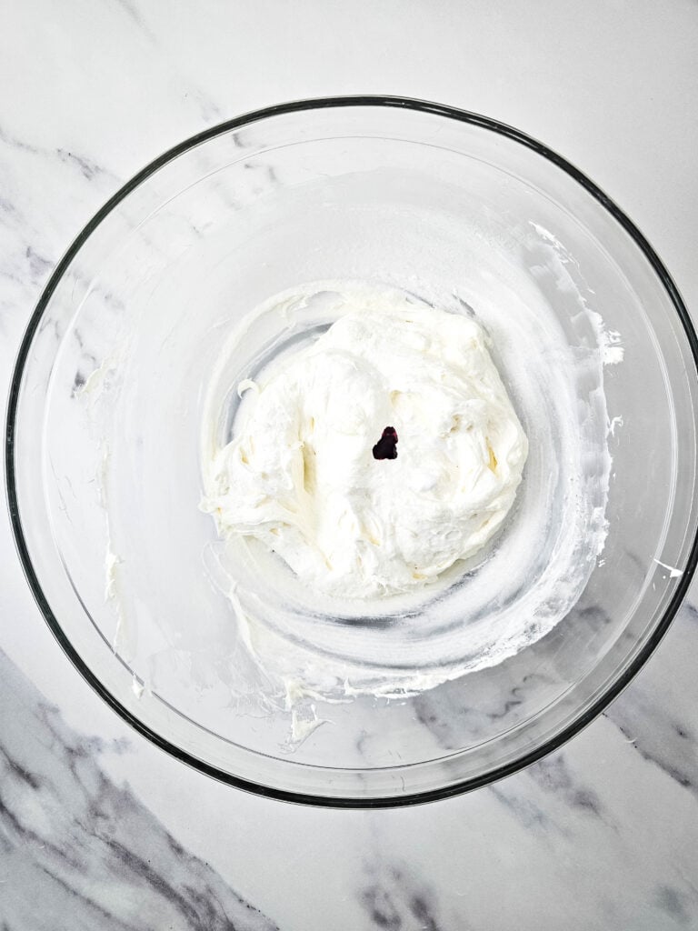 A glass bowl with white whipped fluff with a drop of food coloring in it.