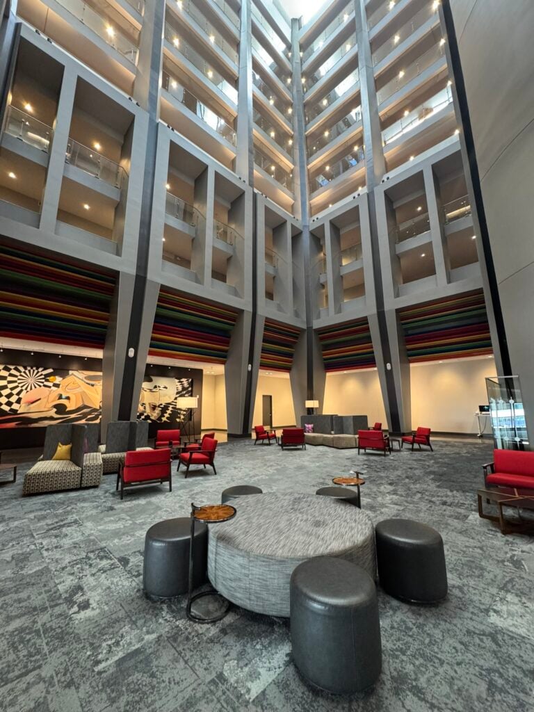 Family-Friendly Hotel in Cincinnati: Our Stay at The Summit Hotel 8 Spacious hotel lobby with modern seating, red chairs, gray ottomans, patterned carpet, tall walls, artwork, and upper floor balconies visible.